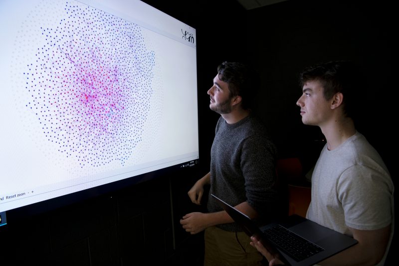 Two male students looking at a data visualization on a large screen.