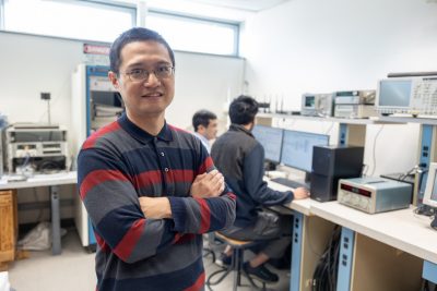 Lingjia Liu stands in Wireless@VT lab in Blacksburg, Va with students working at computers in the background.