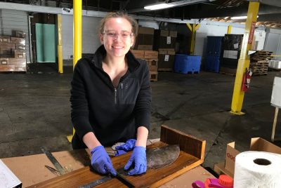 A person stands behind a table, holding a ruler to measure the size of a flounder.