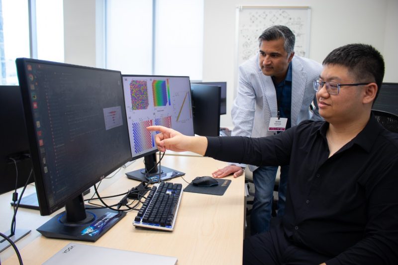 Researchers gathered around a computer screen analyzing research.