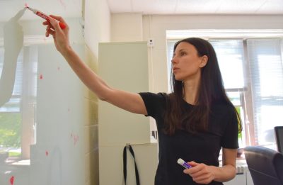 A woman stands at a whiteboard, drawing technical ratios.