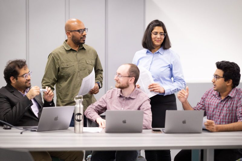 Four researchers gather around a table looking at three computers