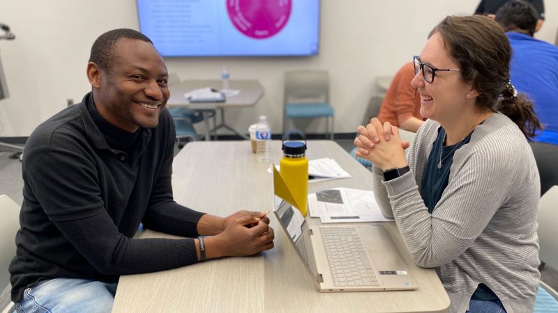 Two students smile as they talk to each other over a table