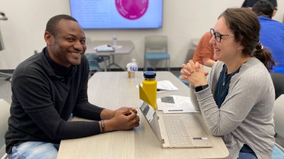 Two students smile as they talk to each other over a table