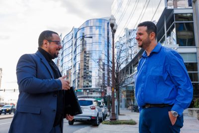 Walid Saad and Omar Hashash stand on a sidewalk in front of buildings.