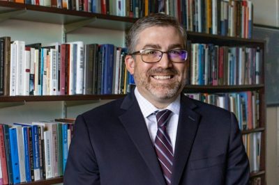 man in suit standing in front of book shelf