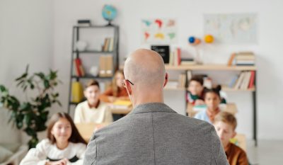 Back of man's head with children sitting at desks in front of him.
