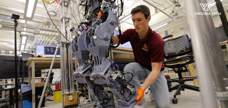 A researcher kneeling down adjusting a leg on a robot.